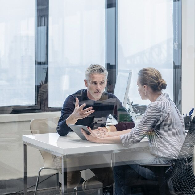 Businessman and businesswoman sitting at desk in modern office, in discussion. Manager gesturing with employee