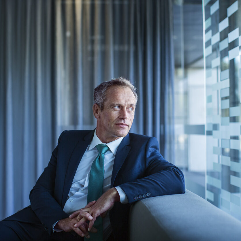 Thoughtful businessman looking out window while sitting on sofa in office lobby